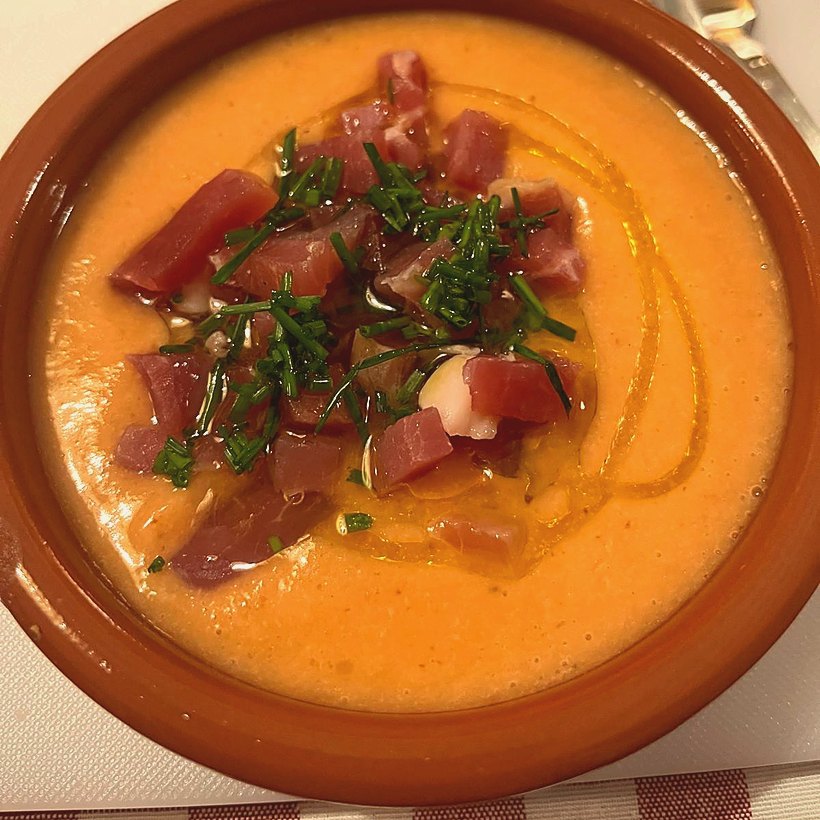 A tapa served in a terracotta dish with cured ham, herbs and a ribbon of olive oil